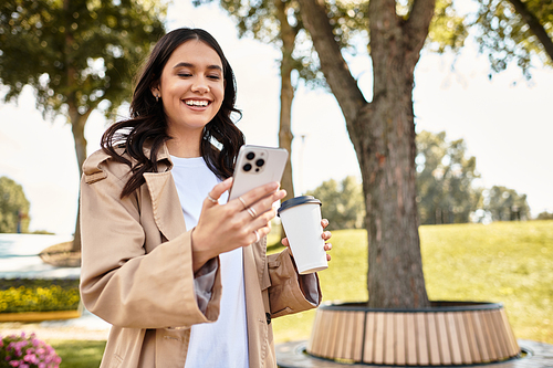 A joyful young woman dressed in cozy autumn attire checks her phone with a warm beverage nearby.