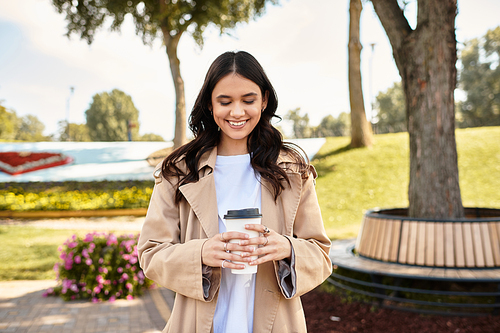 A young beautiful woman smiles warmly while holding a coffee cup, dressed for autumn.