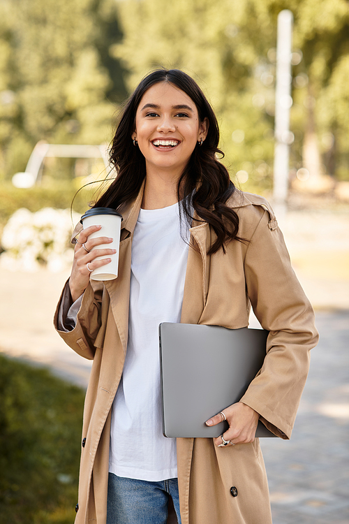 A young woman smiles, strolling through a vibrant park with warm coffee, dressed for autumn.