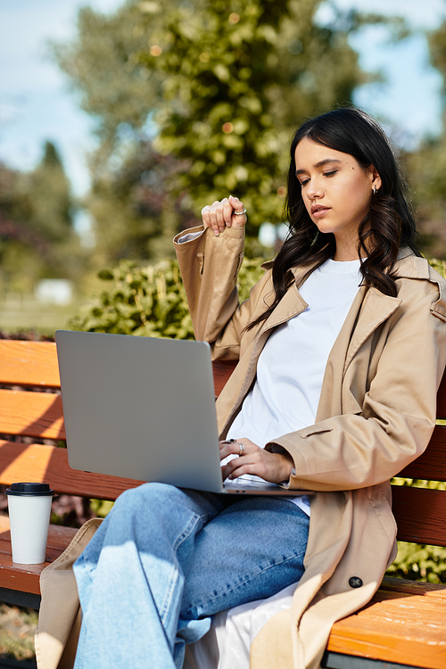 A young woman dressed for autumn is focused on her laptop while enjoying the parks tranquility.