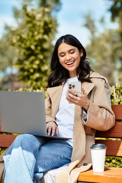 Sitting on a bench, a young woman in cozy autumn attire laughs while checking her phone in the park.