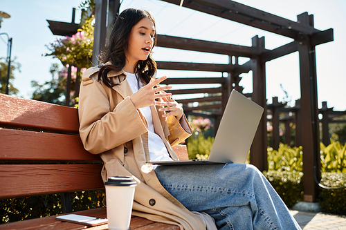 Dressed warmly for autumn, a young woman sits on a bench, engaged in her work outdoors.