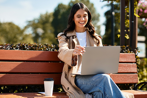 Dressed in warm attire, a woman smiles as she works on her laptop in an autumn park.