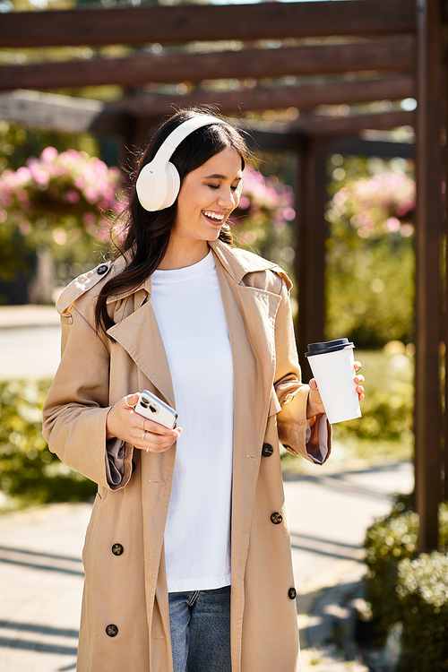 A cheerful young woman in stylish autumn attire walks through a vibrant park, sipping coffee.