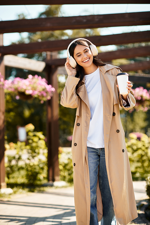 A young woman in cozy autumn attire strolls through a park, sipping her coffee with joy.