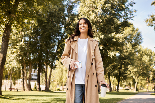 Basking in the beauty of autumn, a young woman walks through the park, sipping coffee.