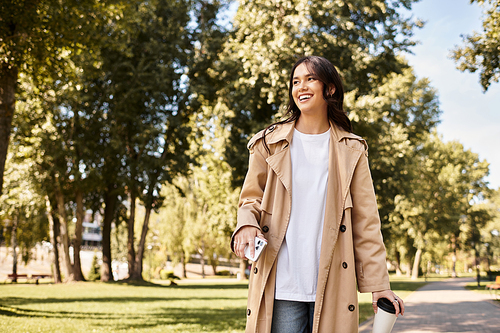 A young woman in cozy autumn attire wanders through a vibrant park filled with golden leaves.