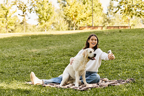 A young woman enjoys a sunny autumn day in the park while taking a selfie with her dog.