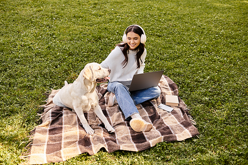 In a serene park, a young woman in warm attire works on her laptop, sharing joy with her dog.