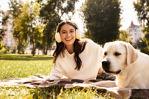 A cheerful woman in cozy autumn clothing relaxes outdoors with her dog, soaking up the sun.