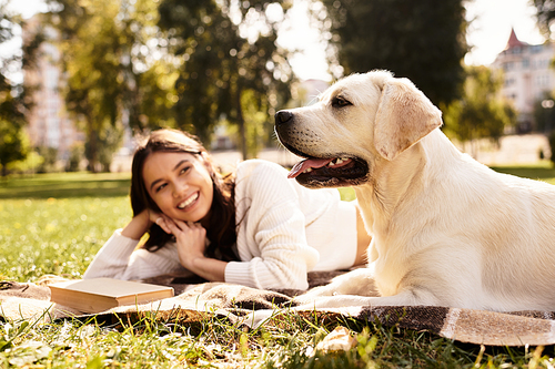 A young woman relaxes on a blanket in the park, enjoying the warm autumn day with her dog.