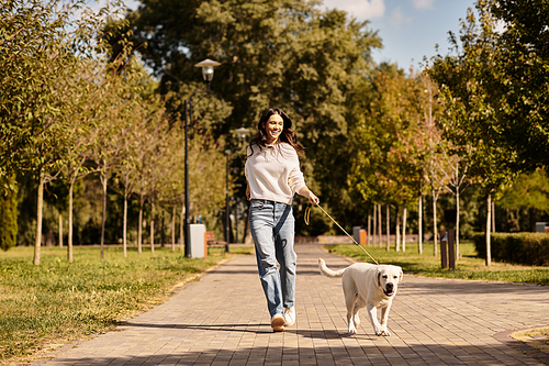 A young woman enjoys a pleasant walk in a picturesque autumn park with her playful dog.