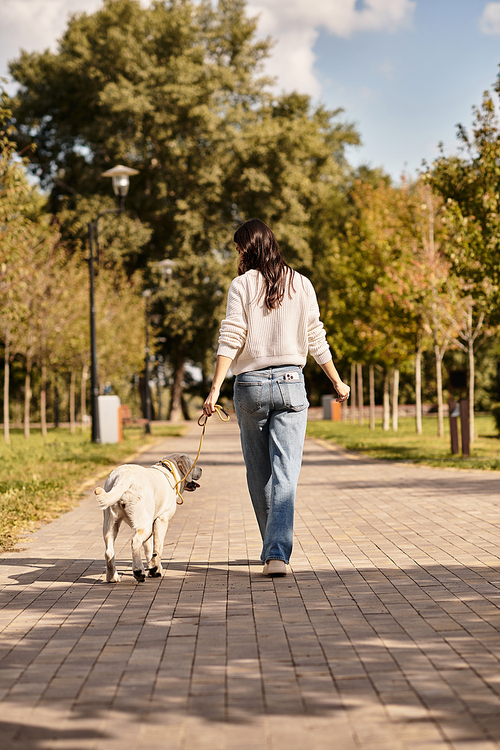 A beautiful woman dressed in cozy autumn attire strolls through a park with her dog.