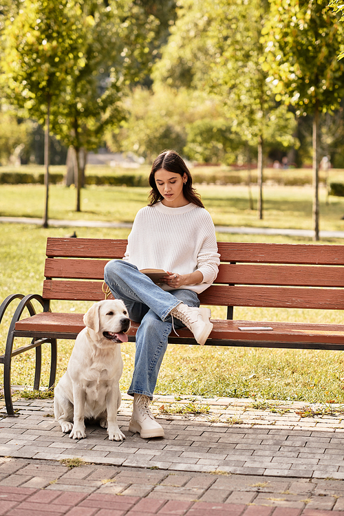 A beautiful woman in cozy autumn attire sits on a bench, reading with her dog by her side.