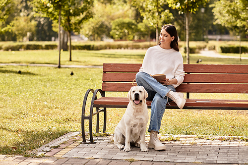 A woman in cozy autumn attire relaxes on a bench, sharing a moment with her dog in the park.