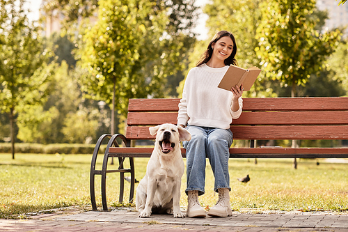 As golden leaves fall, a young woman sits on a bench, absorbed in her book with her dog by her side.