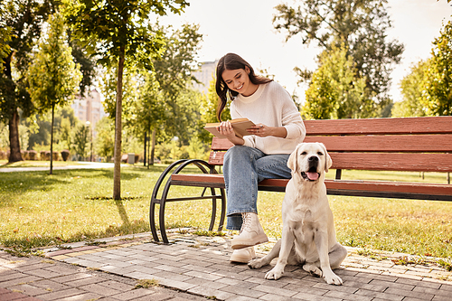 In a sunlit park, a young woman sits on a bench, cherishing time with her dog.