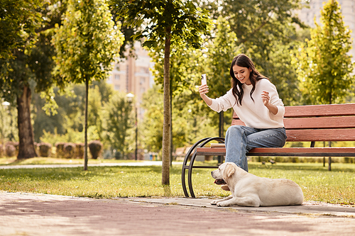 A young woman enjoys a sunny day, capturing memories with her dog in a lush park.