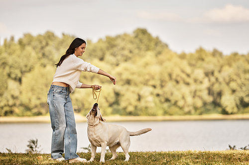 A young woman in cozy autumn attire plays joyfully with her dog near a serene lake.