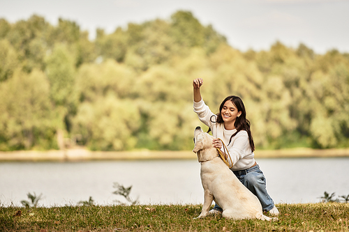 A young woman dressed in cozy autumn attire interacts joyfully with her dog near a serene lake.