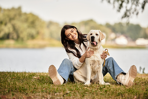 Amidst vibrant autumn colors, a woman smiles brightly while petting her dog in a serene park.