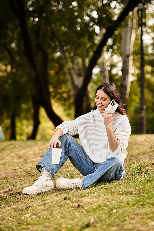 A beautiful young woman sits on the grass, enjoying a conversation and autumn scenery.