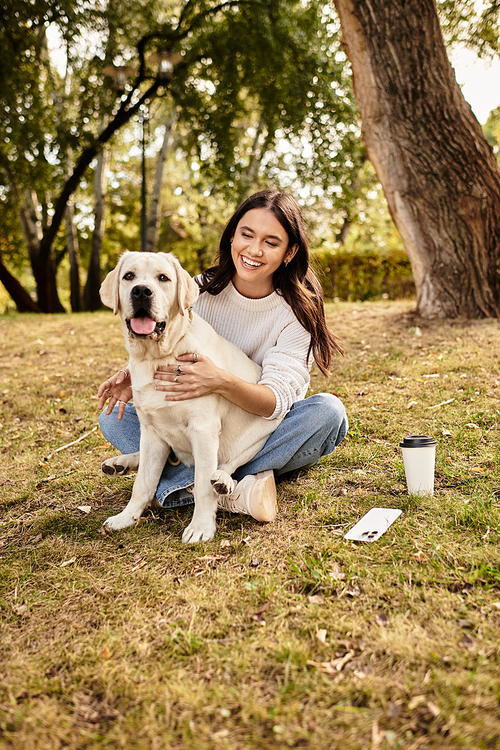 A cheerful woman in cozy autumn clothing embraces her happy dog while relaxing outdoors.