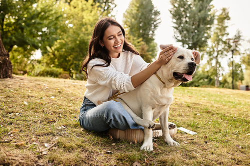 A happy woman in cozy autumn attire plays with her dog under the golden trees.