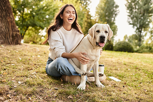 A cheerful woman in cozy autumn attire laughs while playing with her dog in a lovely park.