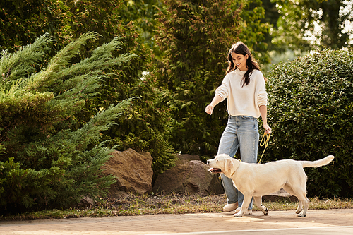 A beautiful woman dressed for autumn walks joyfully with her dog amidst vibrant fall foliage.