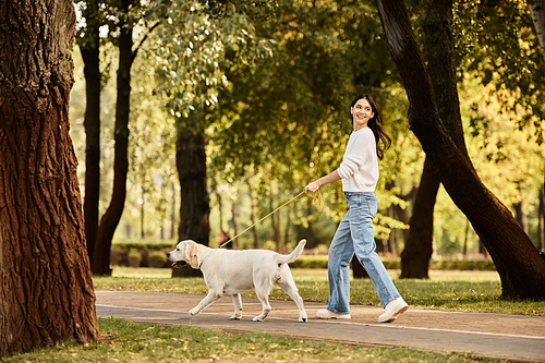 A young woman enjoys a lively walk with her dog on a beautiful autumn day in the park.