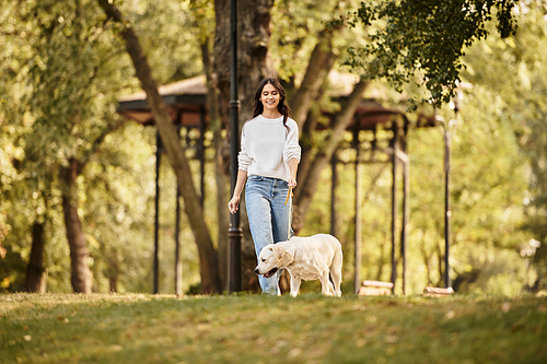 A beautiful young woman walks joyfully with her dog, surrounded by vibrant autumn foliage.