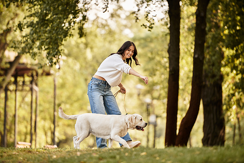 A young woman dressed in warm autumn attire happily strolls with her dog in the park.