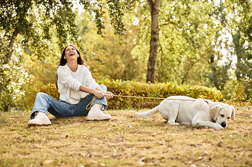 A cheerful woman dressed for autumn laughs while playing with her dog in a lovely park.