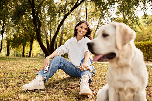 The woman sits on the grass in a park, smiling and enjoying the beautiful autumn weather.