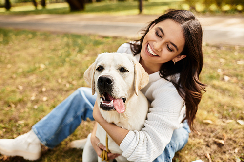 A young woman in cozy autumn attire shares a joyful moment with her dog in a sunlit park.