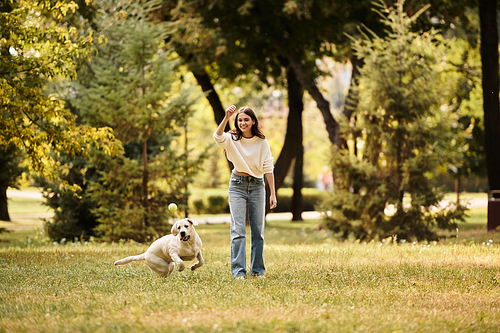 A joyful woman wears cozy autumn attire while frolicking with her dog in a leafy park.