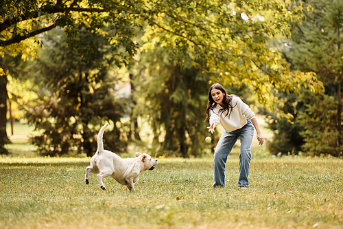 A beautiful woman dressed for autumn interacts with her joyful dog in a vibrant green park.