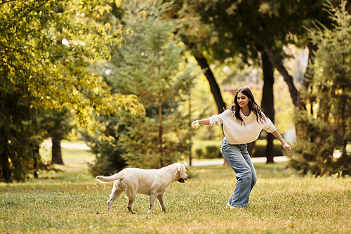 A cheerful young woman in cozy autumn attire plays with her dog in a vibrant park.