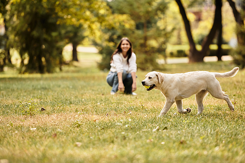 In a vibrant park, a young woman kneels on the grass, smiling joyfully as her dog plays nearby.