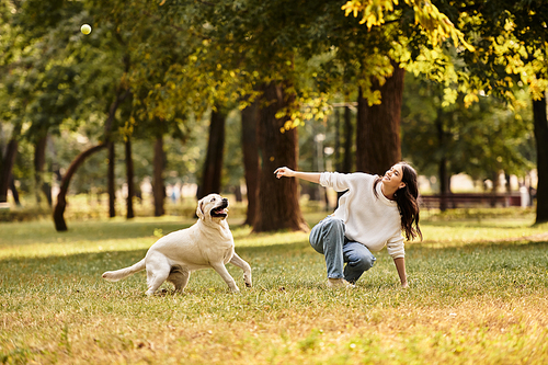 A young woman dressed for autumn enjoys a playful moment with her dog in a beautiful park.