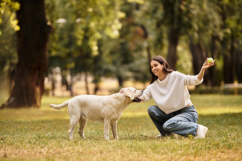 A young woman dressed in cozy autumn attire enjoys a playful interaction with her dog in the park.