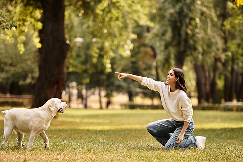 A beautiful woman in warm autumn attire kneels in a vibrant park, joyfully interacting with her dog.