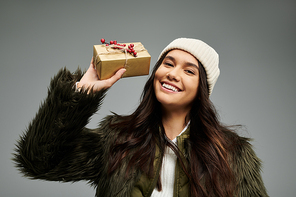 A cheerful young woman showcases a beautifully wrapped gift, radiating joy and warmth.