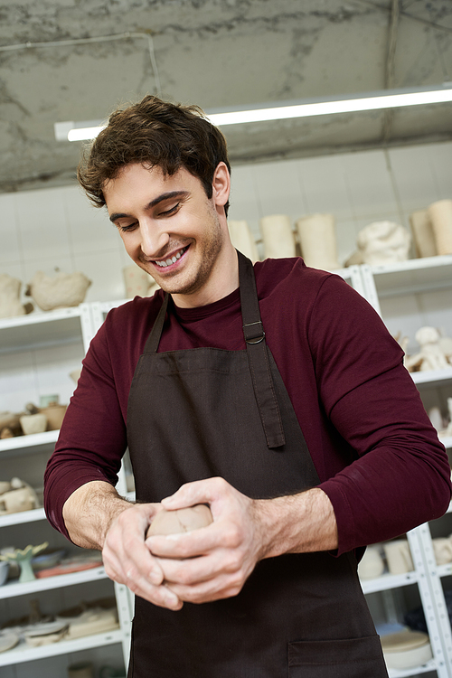 Cheerful handsome man in apron making some pottery in studio.