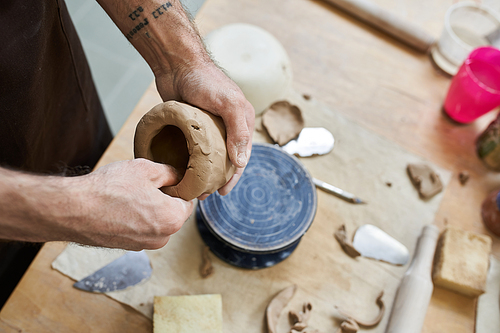 Cheerful talented man in apron making some pottery in studio.