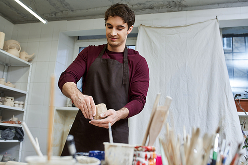 Sophisticated appealing man in apron making some pottery in studio.