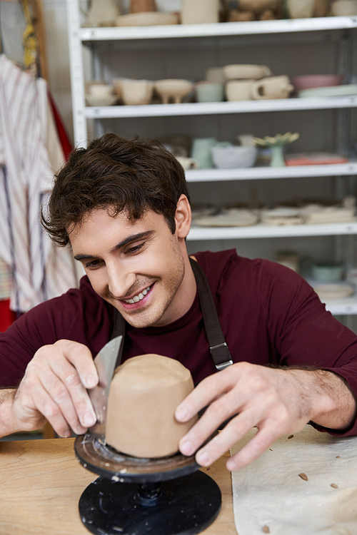 Sophisticated merry man in apron making some pottery in studio.