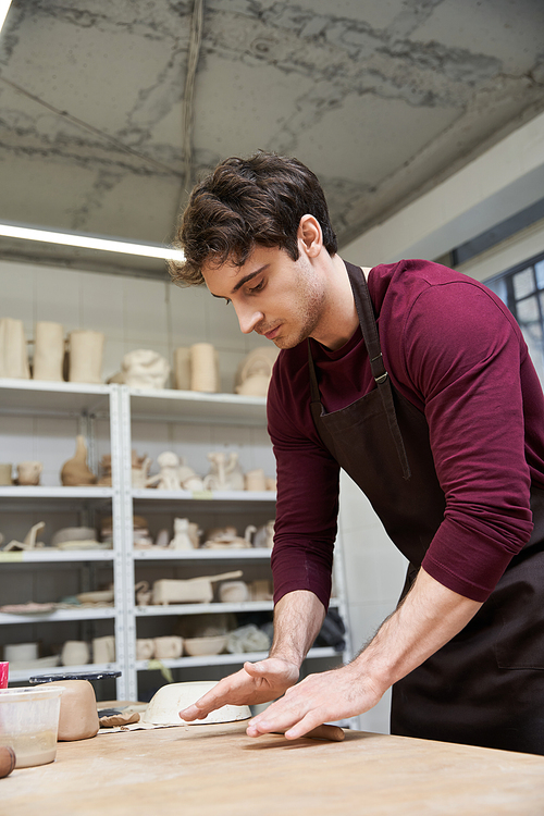 Elegant ambitious man in apron making some pottery in studio.