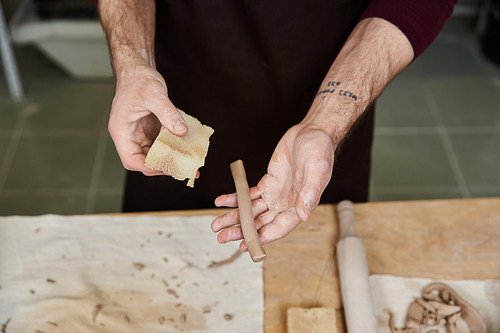 Devoted young man in apron making some pottery in studio.